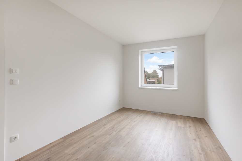 Leerer Raum mit weiß gestrichenen Wänden, Holzfußboden und einem Fenster mit Ausblick.