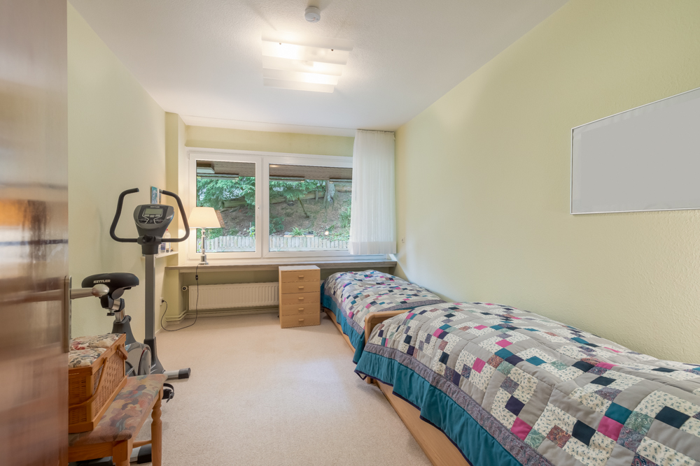 Schlafzimmer mit zwei Einzelbetten, Fenster, Schreibtisch und Heimtrainer.