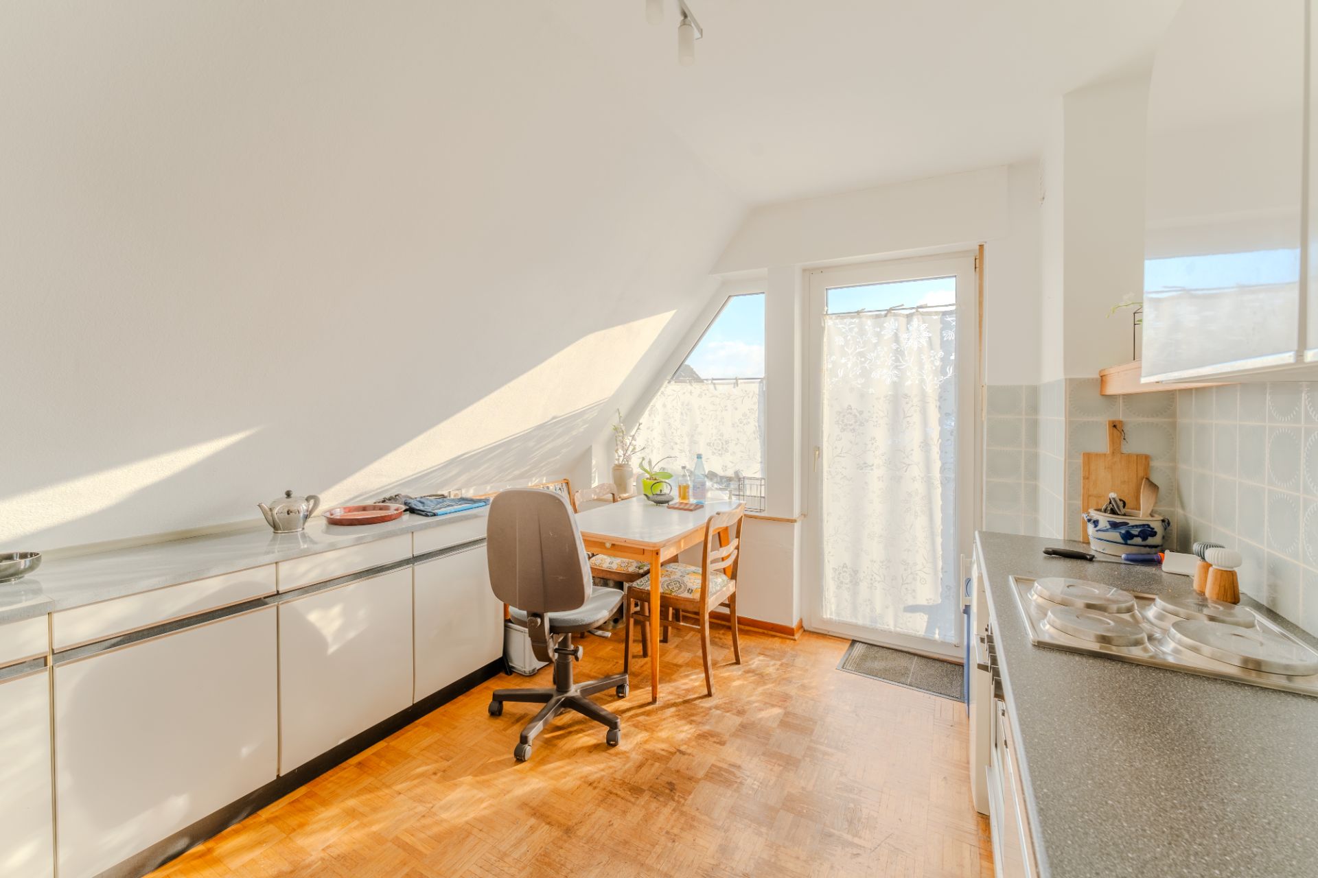 Helle Küche mit Esstisch, zwei Stühlen und Dachschräge, große Fenster bringen Tageslicht herein.