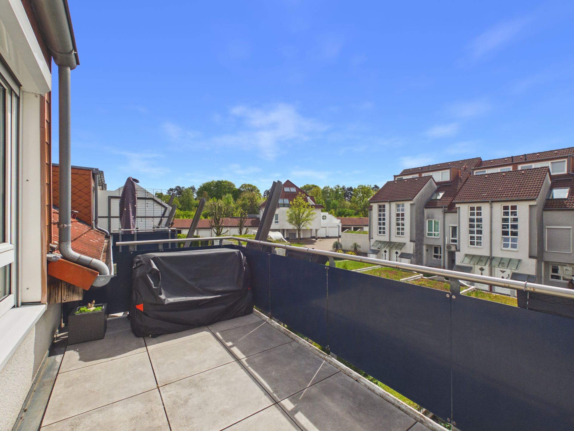 Balkon mit Grillabdeckung, Pflanzkasten und Blick auf Wohnhäuser.