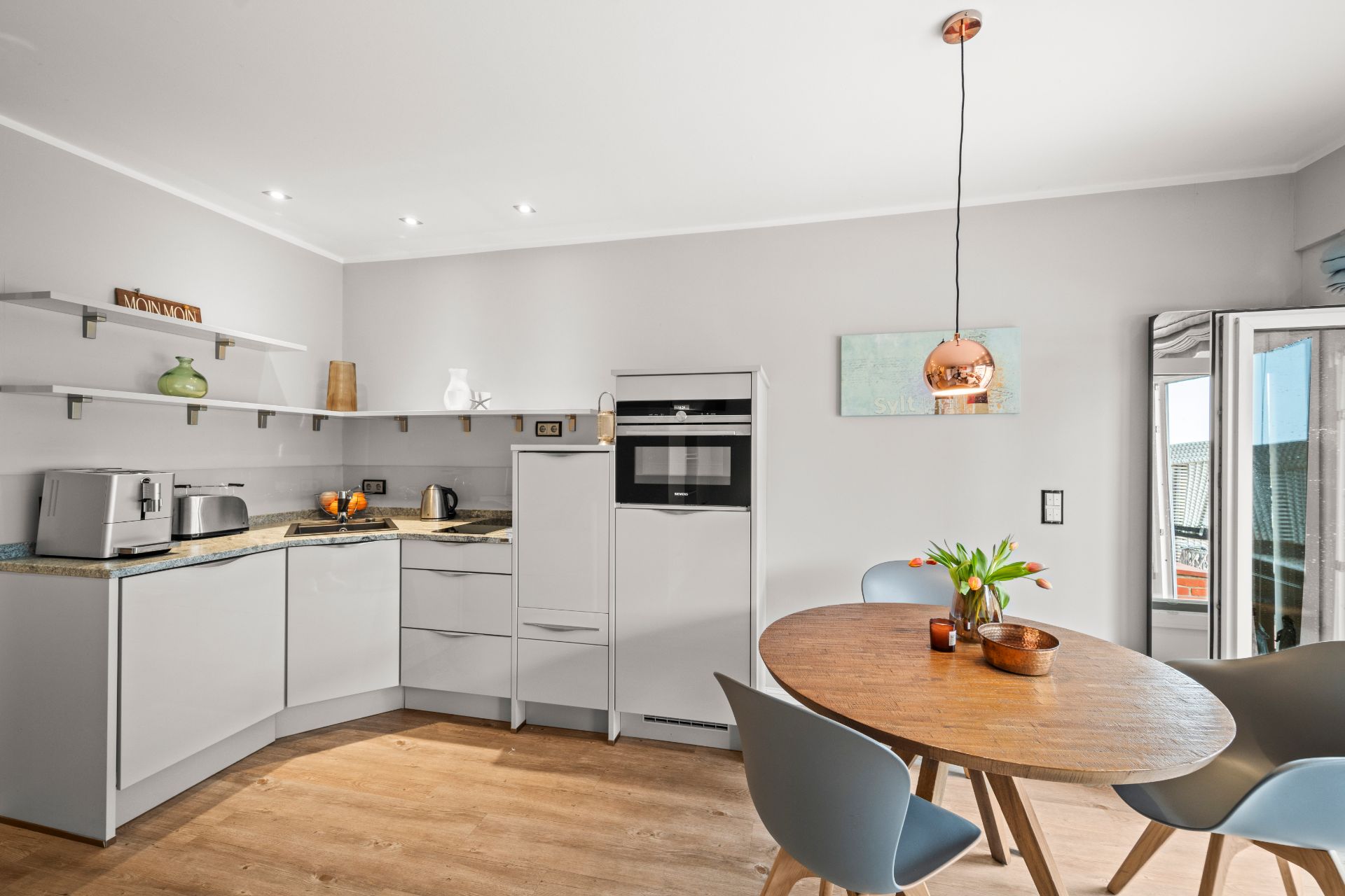 Moderne Küche mit Holztisch, vier Stühlen und offener Tür zum Balkon, helle Einrichtung.