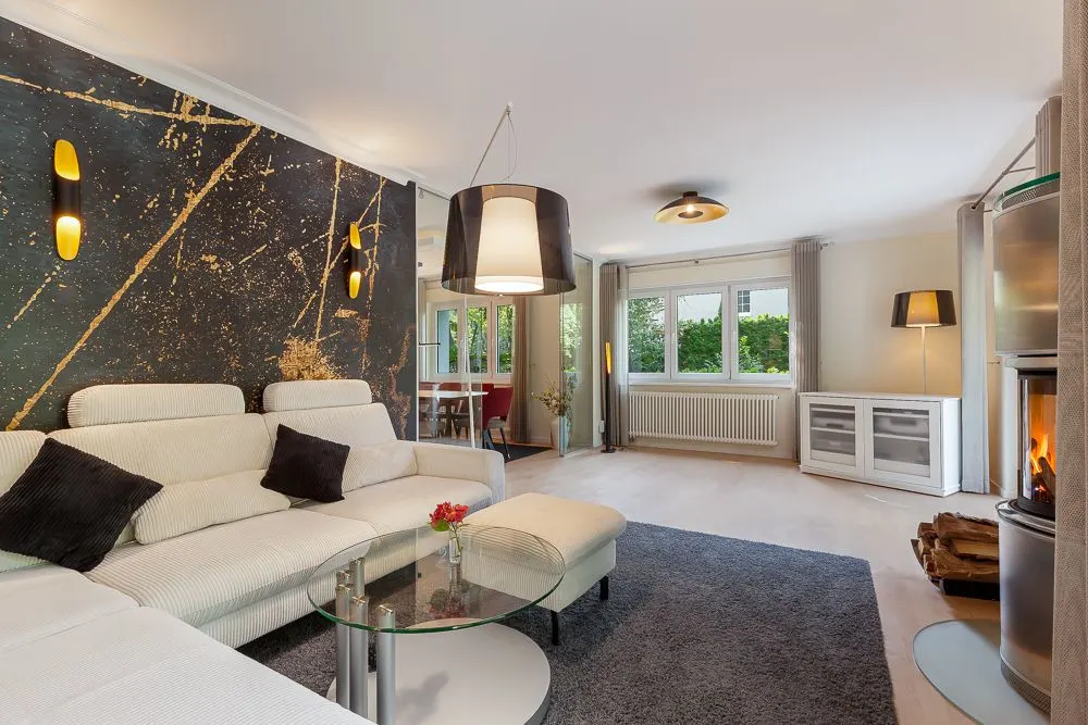 Modernes Wohnzimmer mit weißem Sofa, Glastisch, Kamin und großem Fenster.