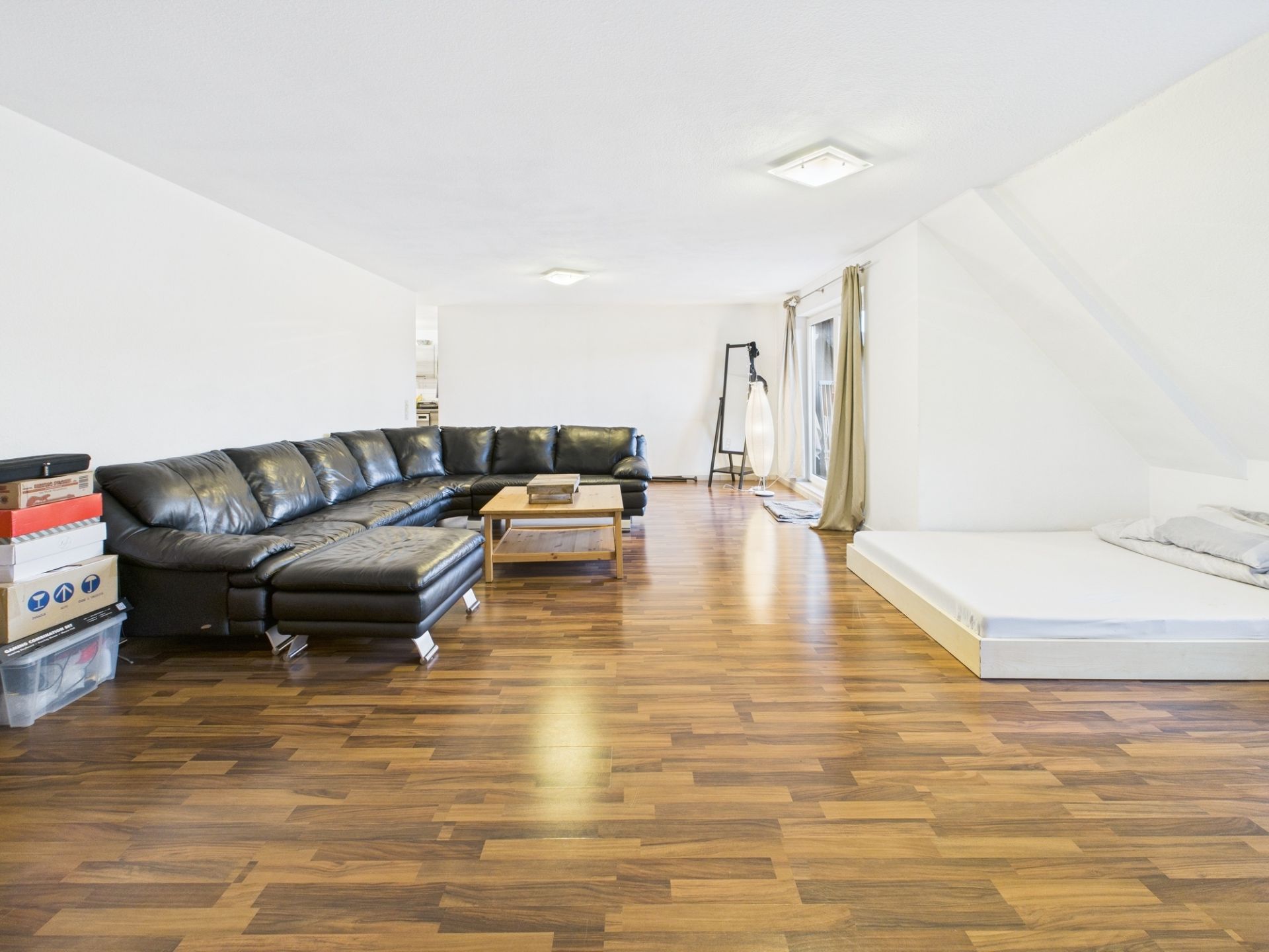 Wohnzimmer mit schwarzem Ecksofa, Couchtisch, Futonbett und Parkettboden.
