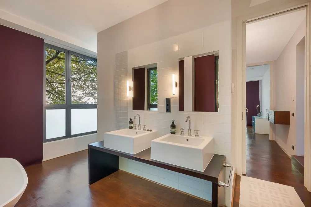 Modernes Badezimmer mit zwei weißen Waschbecken, großem Fenster und dunklem Holzboden.
