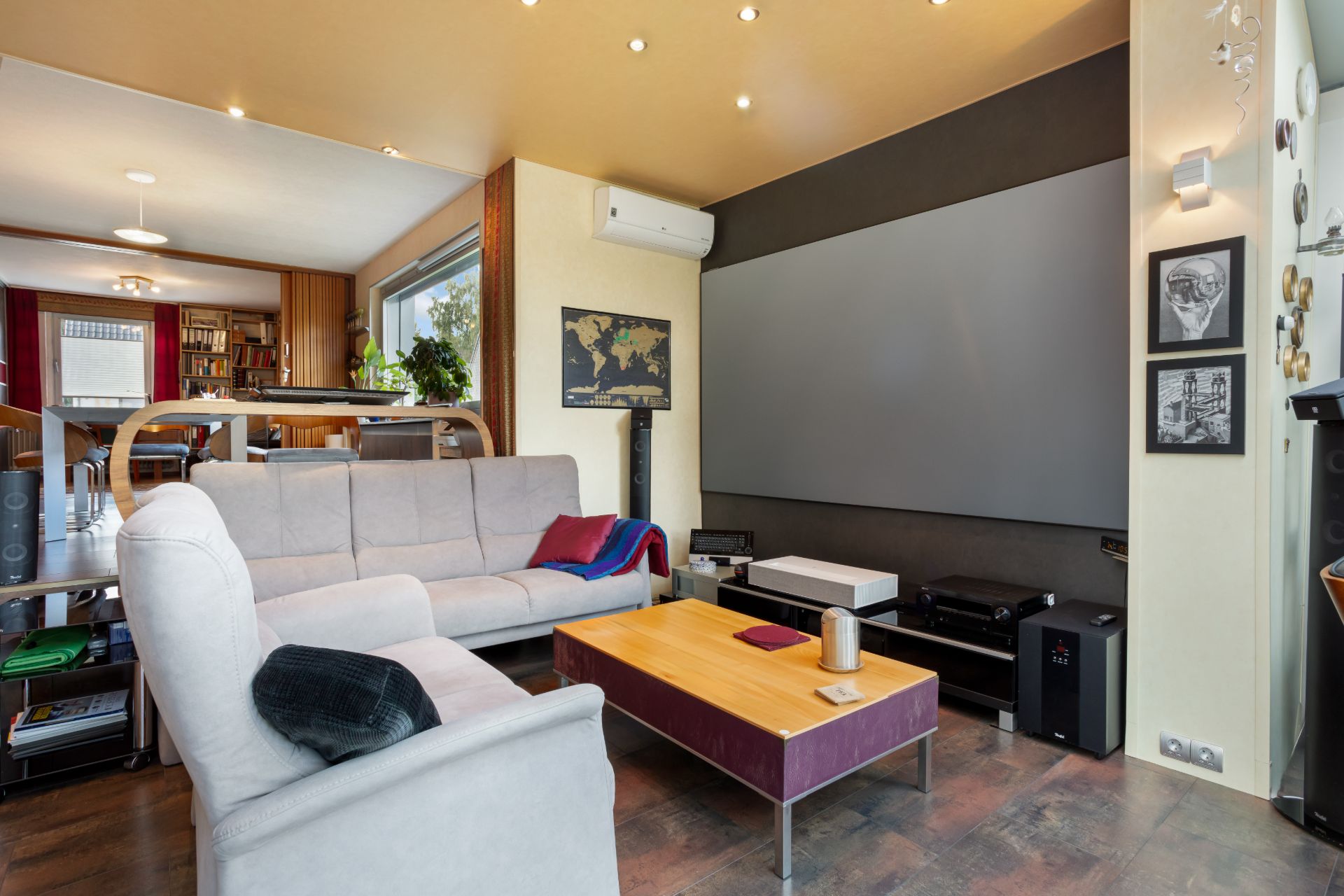 Wohnzimmer mit grauer Couch, Couchtisch und großer Leinwand an der Wand.