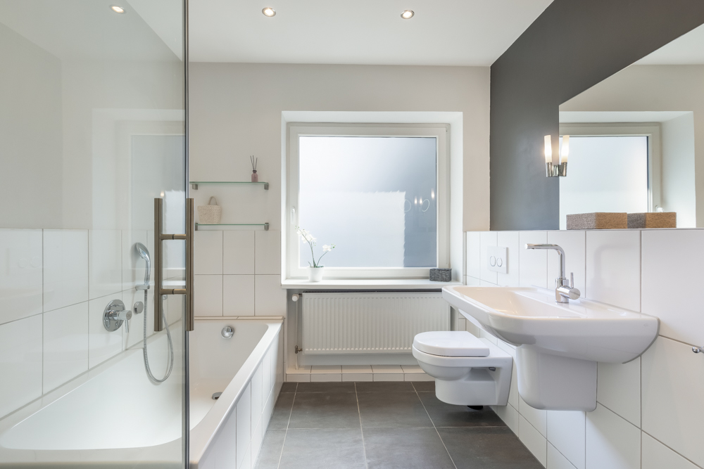 Modernes, helles Badezimmer mit Badewanne, Waschbecken, WC und großem Fenster.