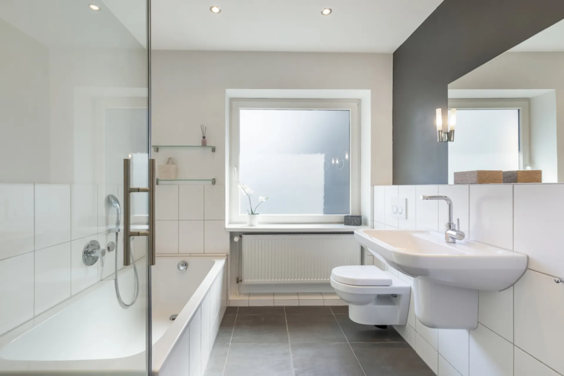 Modernes, helles Badezimmer mit Badewanne, Waschbecken, WC und großem Fenster.