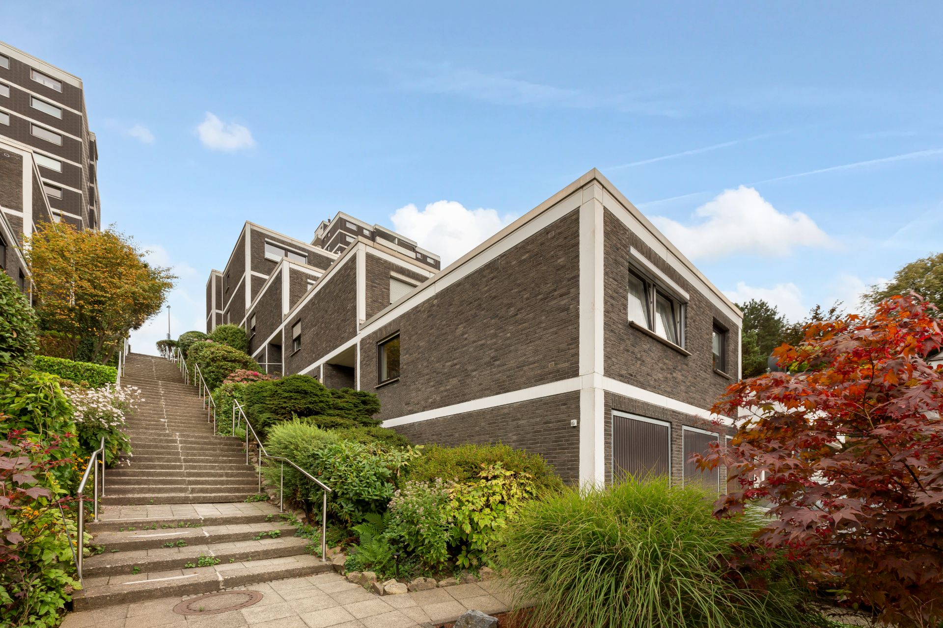 Moderne Mehrfamilienhäuser mit dunkler Fassade und Treppe, umgeben von grüner Bepflanzung.
