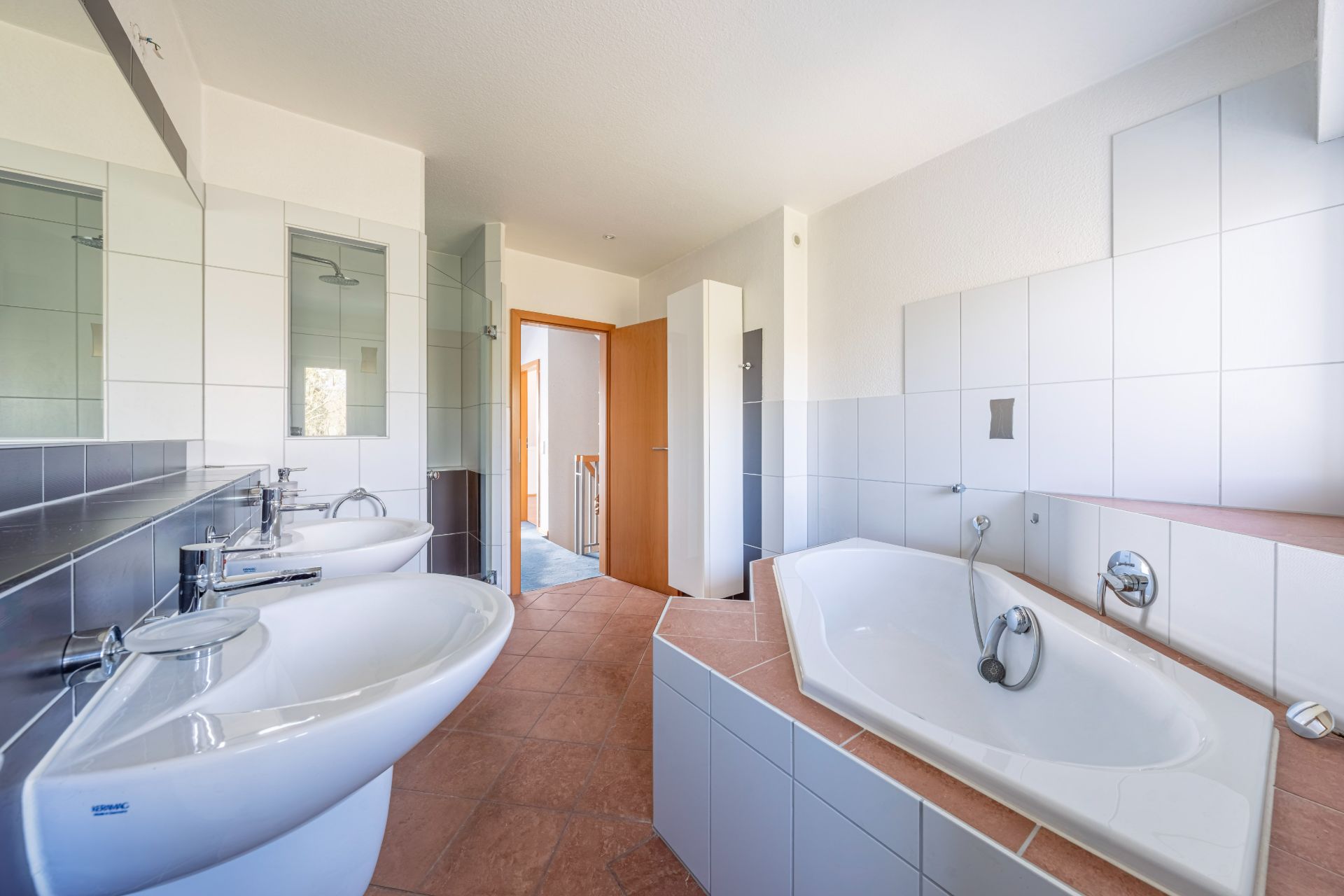 Modernes Badezimmer mit zwei Waschbecken, Eckbadewanne und Fliesen an Wänden und Boden.