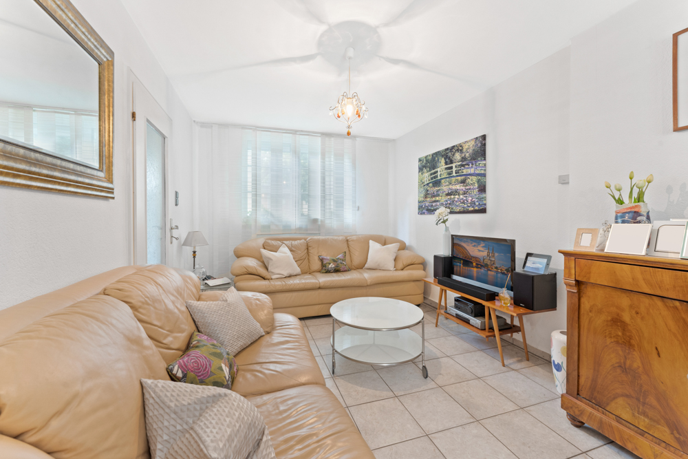 Helles Wohnzimmer mit beigen Sofas, Glastisch, Sideboard und großen Fenstern.