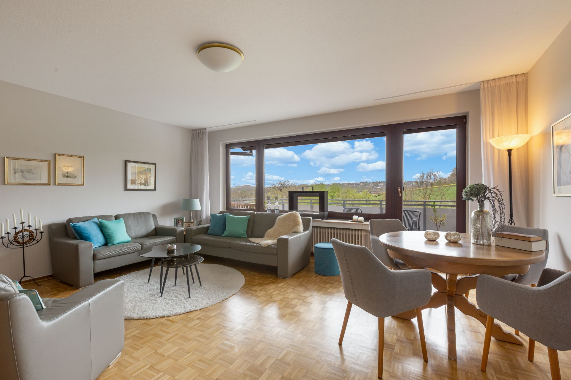 Helles Wohnzimmer mit zwei Sofas, Esstisch und großem Fenster mit Blick ins Grüne.