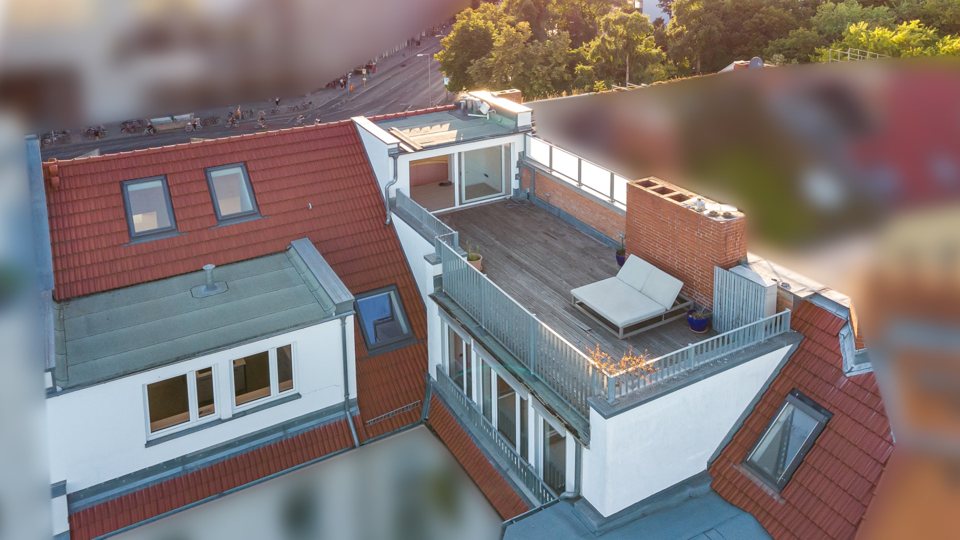 Dachterrasse mit Liege und Geländer auf einem Wohngebäude mit roten Dachziegeln.