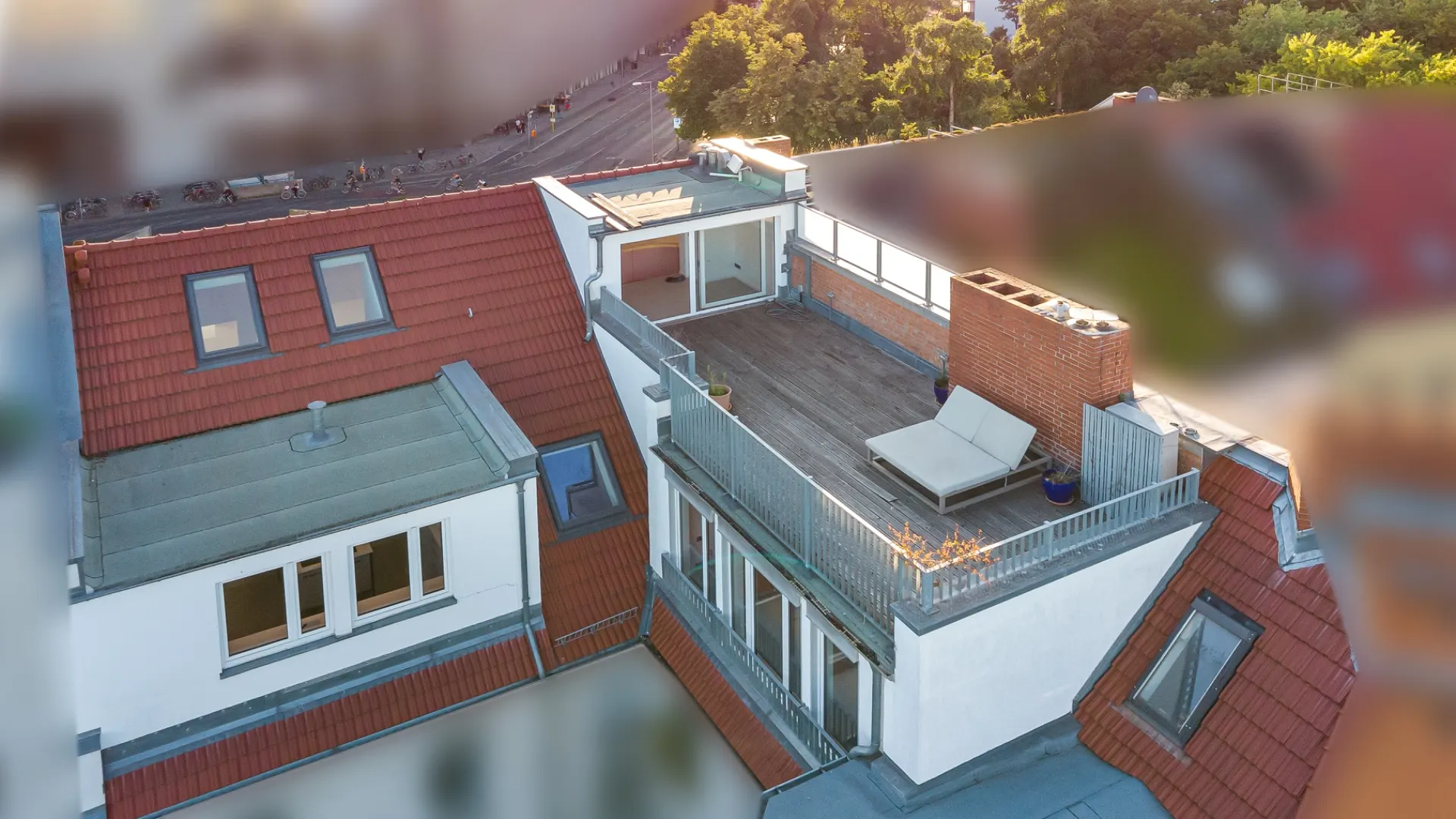 Dachterrasse mit Liege und Geländer auf einem Wohngebäude mit roten Dachziegeln.