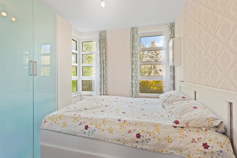 Helles Schlafzimmer mit großem Fenster, Doppelbett und hellblauem Kleiderschrank.