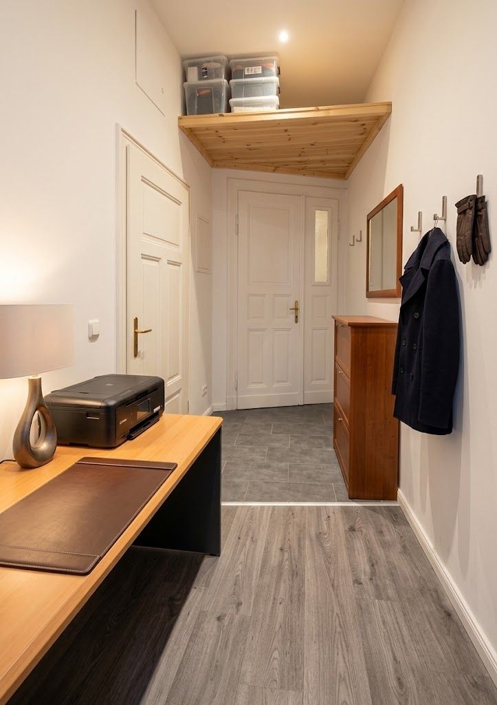 Flur mit Schreibtisch, Drucker, Kommode, Garderobe und Abstellfläche mit Boxen oben.