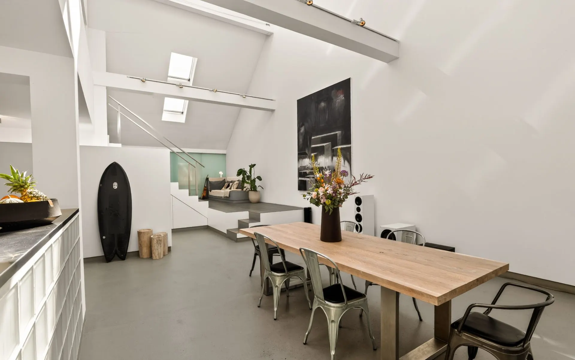 Heller Essbereich mit Holztisch, Metallstühlen, Surfbrett und Sitznische in modernem Wohnraum.