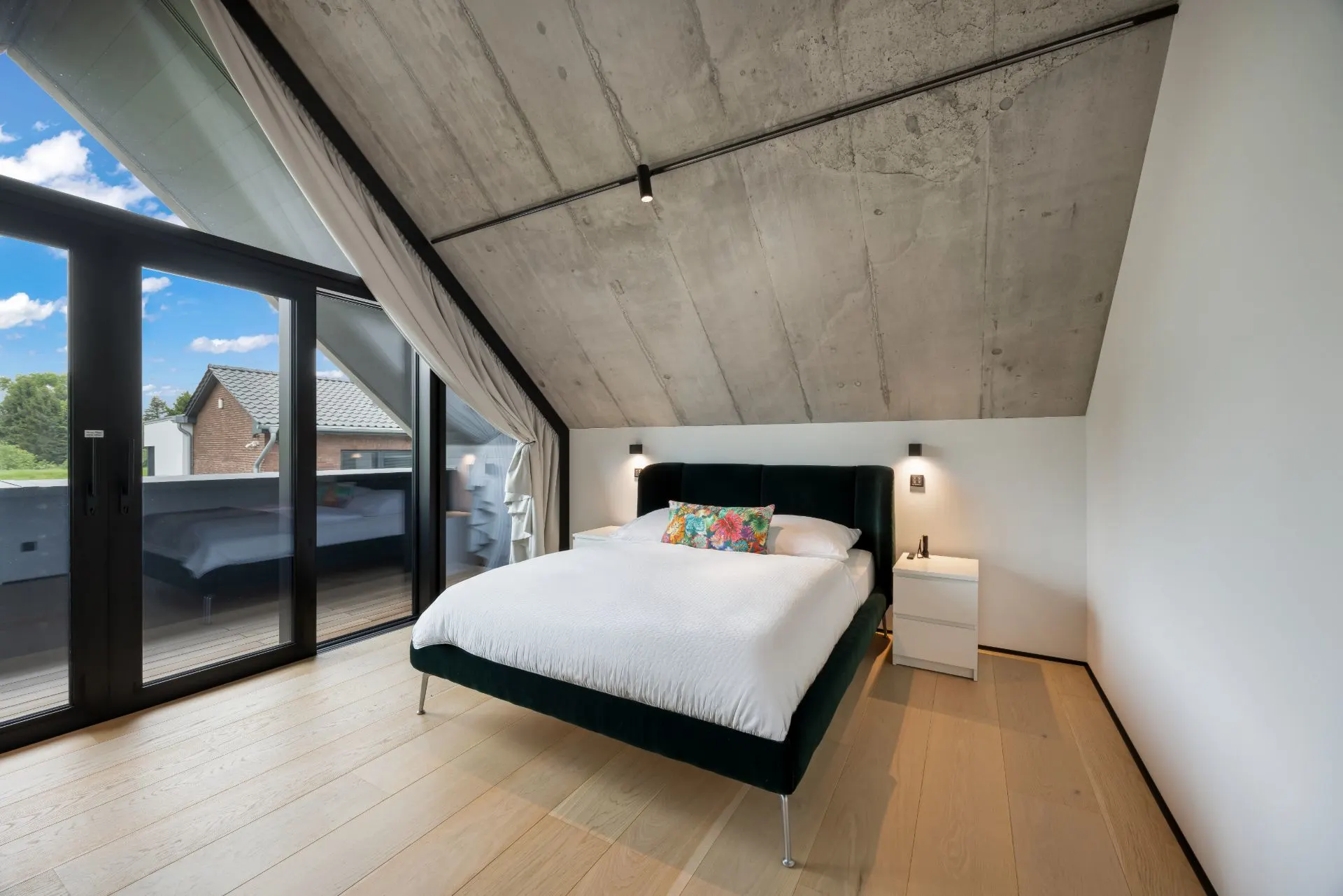 Modernes Schlafzimmer mit Doppelbett, Nachttischen, Holzfußboden und Zugang zu einem Balkon.