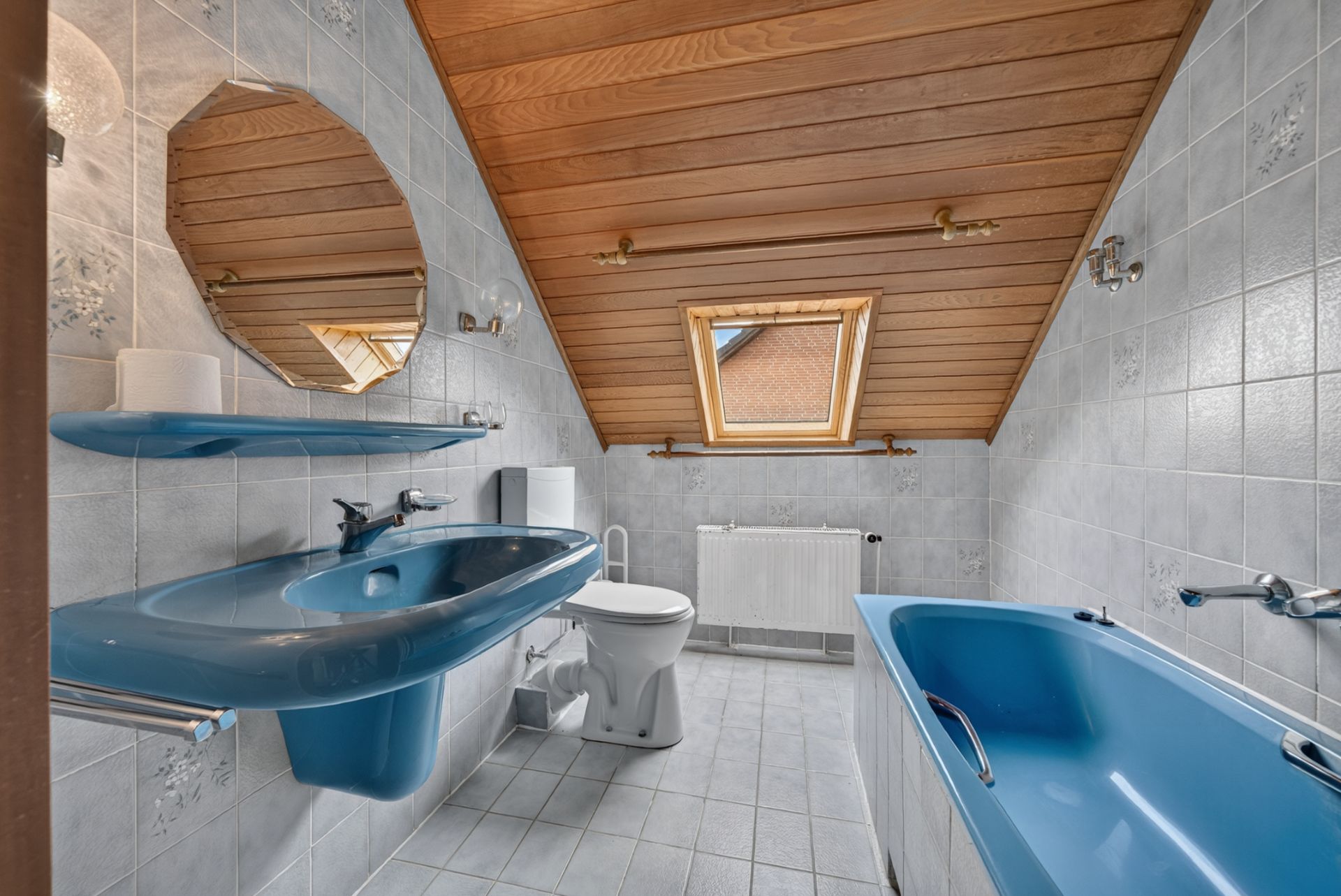 Badezimmer mit blauer Badewanne, blauem Waschbecken, Toilette und Dachfenster.