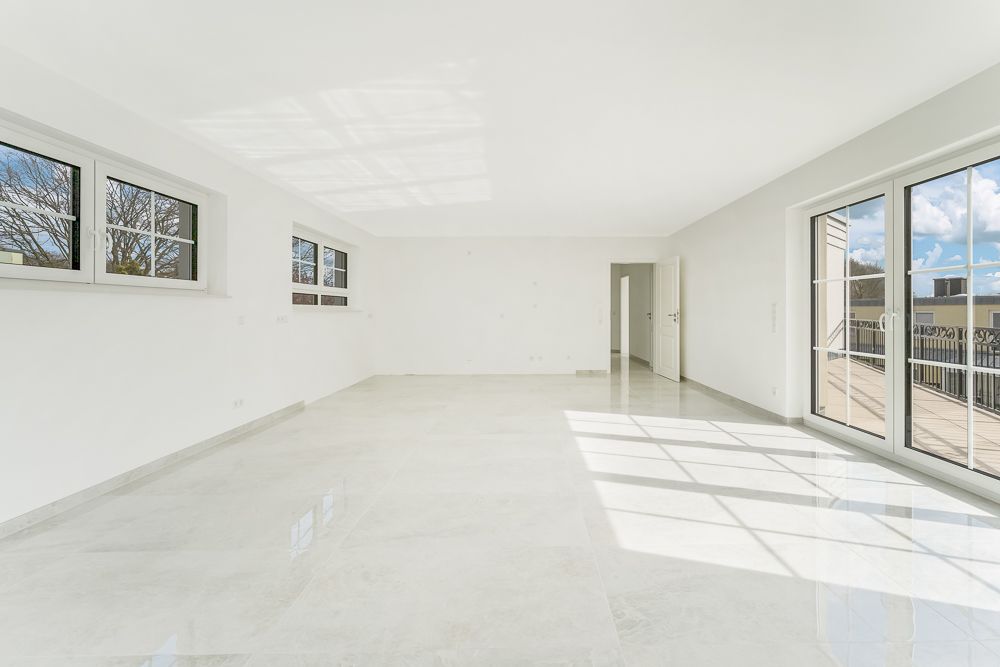 Heller, leerer Raum mit großen Fenstern und Glastüren zu einem Balkon.