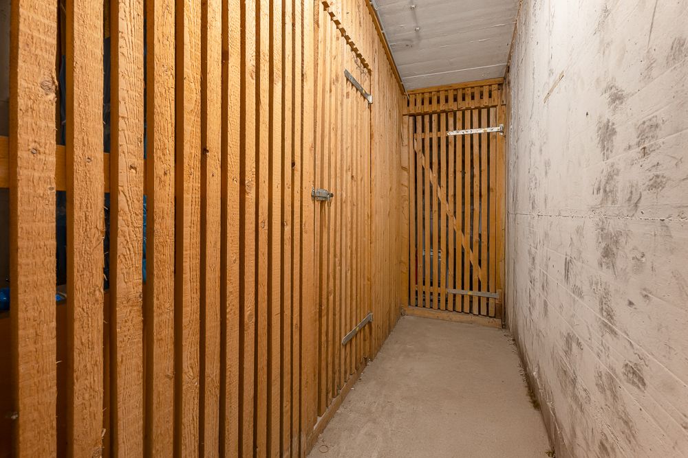 Schmaler Kellerraum mit Holzgitterwänden und verschlossener Holztür.