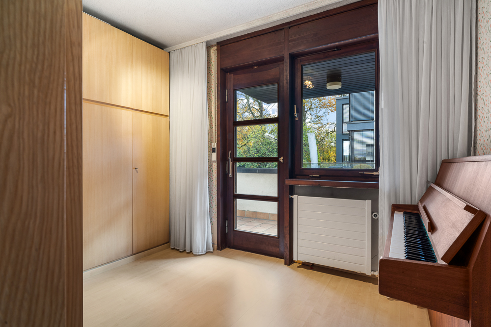 Heller Raum mit großem Holzschrank, Klavier und Tür zum Balkon.