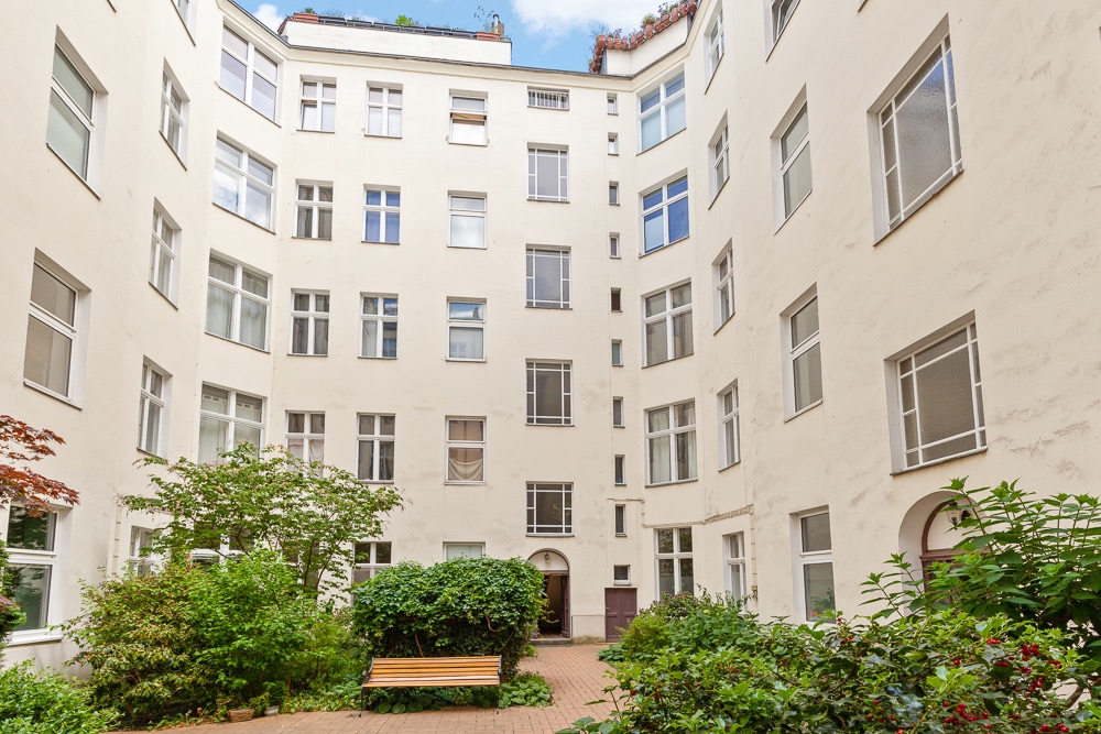 Innenhof eines Wohngebäudes mit Pflanzen, Büschen und einer Holzbank.