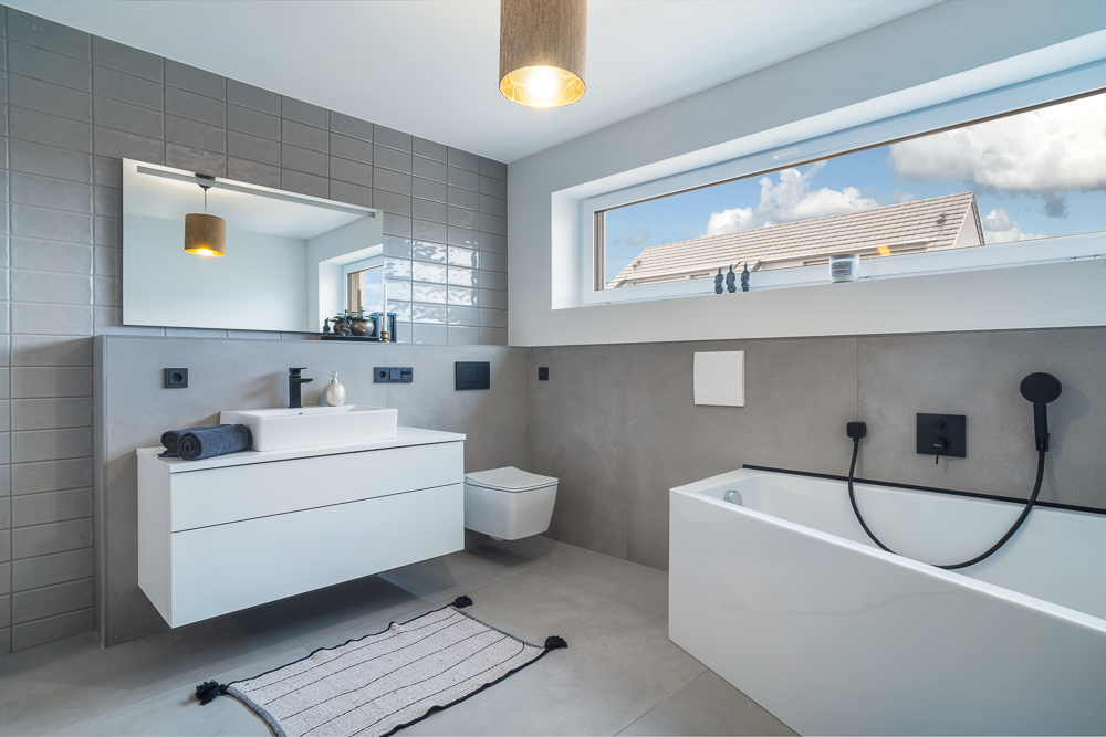 Modernes Badezimmer mit Badewanne, Wandwaschbecken, Spiegel, Fenster und Hänge-WC.