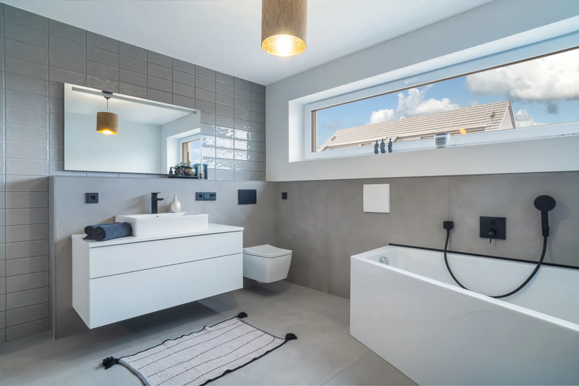 Modernes Badezimmer mit Badewanne, Wandwaschbecken, Spiegel, Fenster und Hänge-WC.