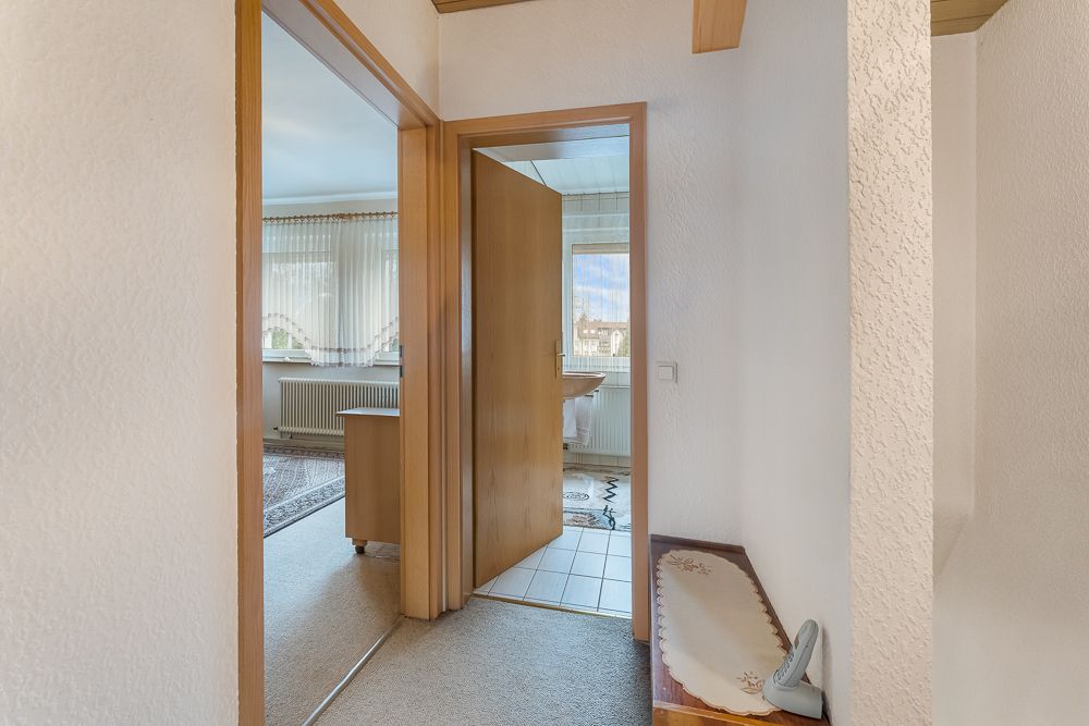 Flur mit Blick in ein Zimmer und ein Badezimmer, helle Wände und Holztüren.