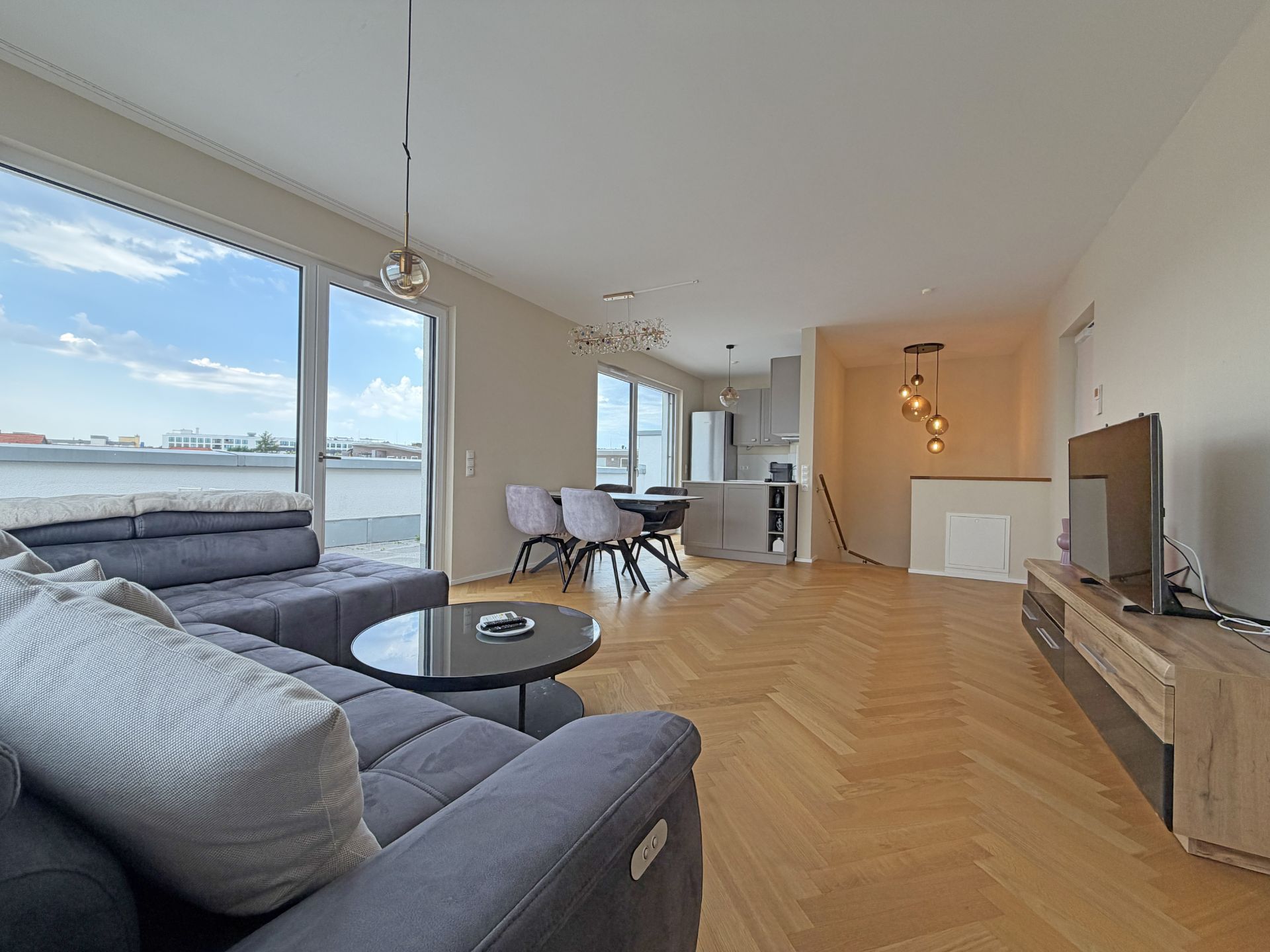 Modernes Wohnzimmer mit Ecksofa, Esstisch, großen Fenstern und offener Küche.