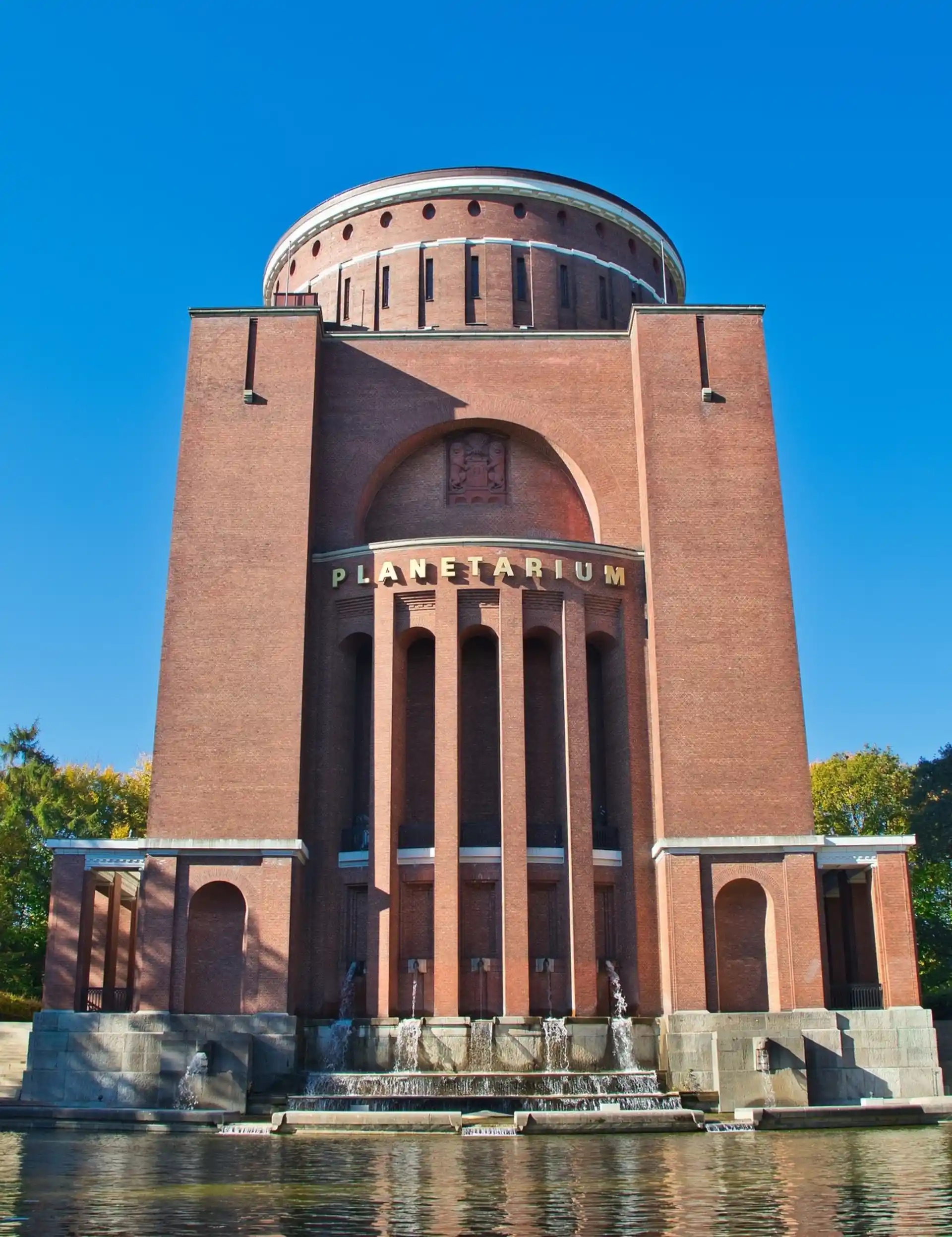 Backsteingebäude mit Säulen, Wasserbecken und dem Schriftzug 'Planetarium' an der Fassade.