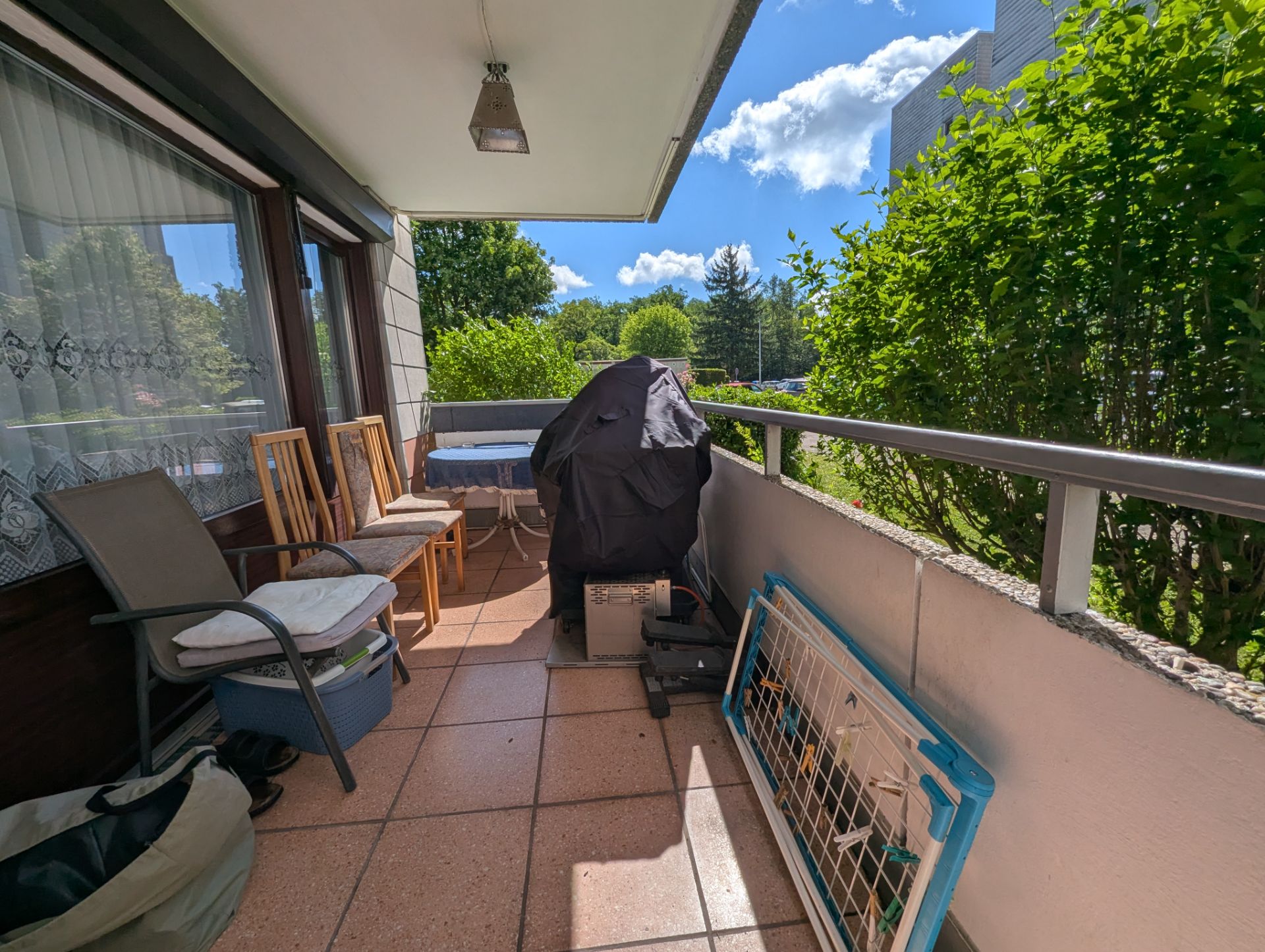 Möblierter Balkon mit Stuhl, Tisch, Grill und Pflanzen an der Seite.