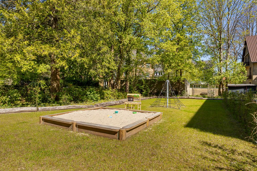 Garten mit Sandkasten, Spielzeug und Klettergerüst umgeben von Bäumen.