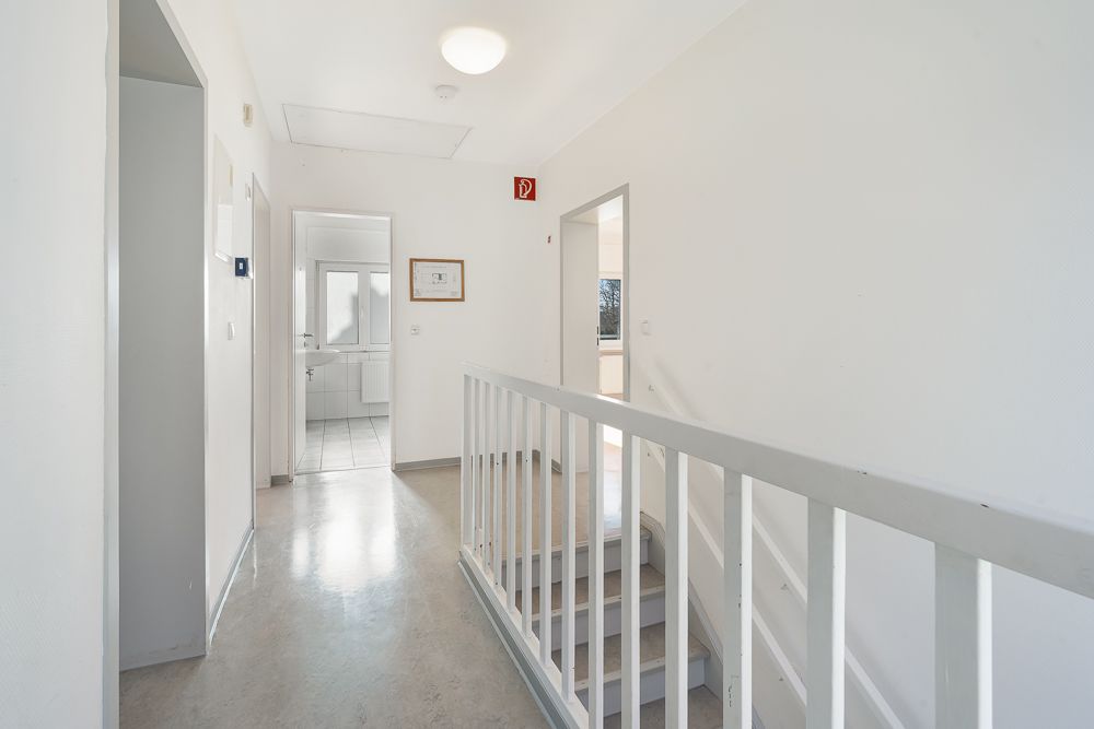 Heller Flur mit Treppe, weißen Wänden und Türen zu angrenzenden Zimmern.