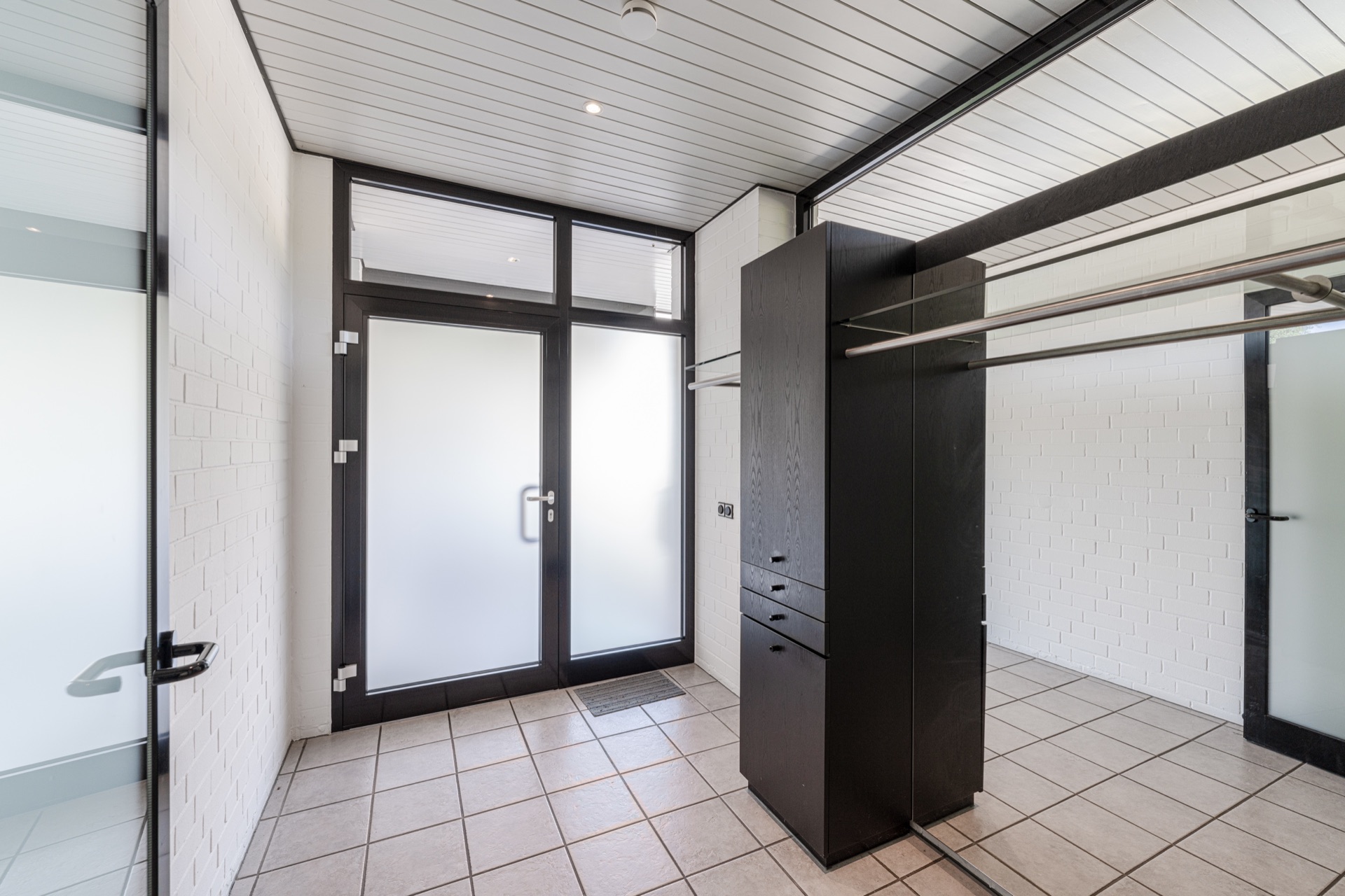 Heller Raum mit Fliesenboden, Einbauschrank und großen Glastüren mit Milchglas.