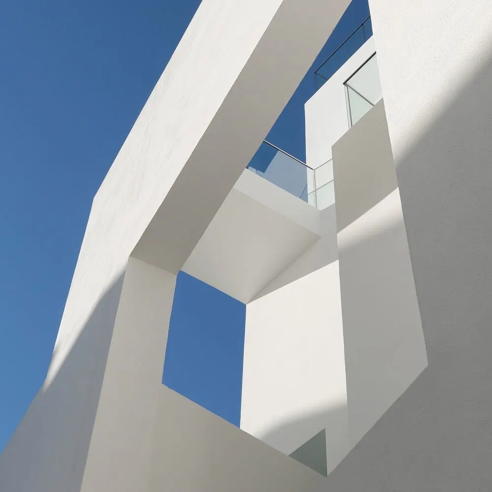 Moderne weiße Gebäudewinkel mit Glasgeländer vor blauem Himmel.