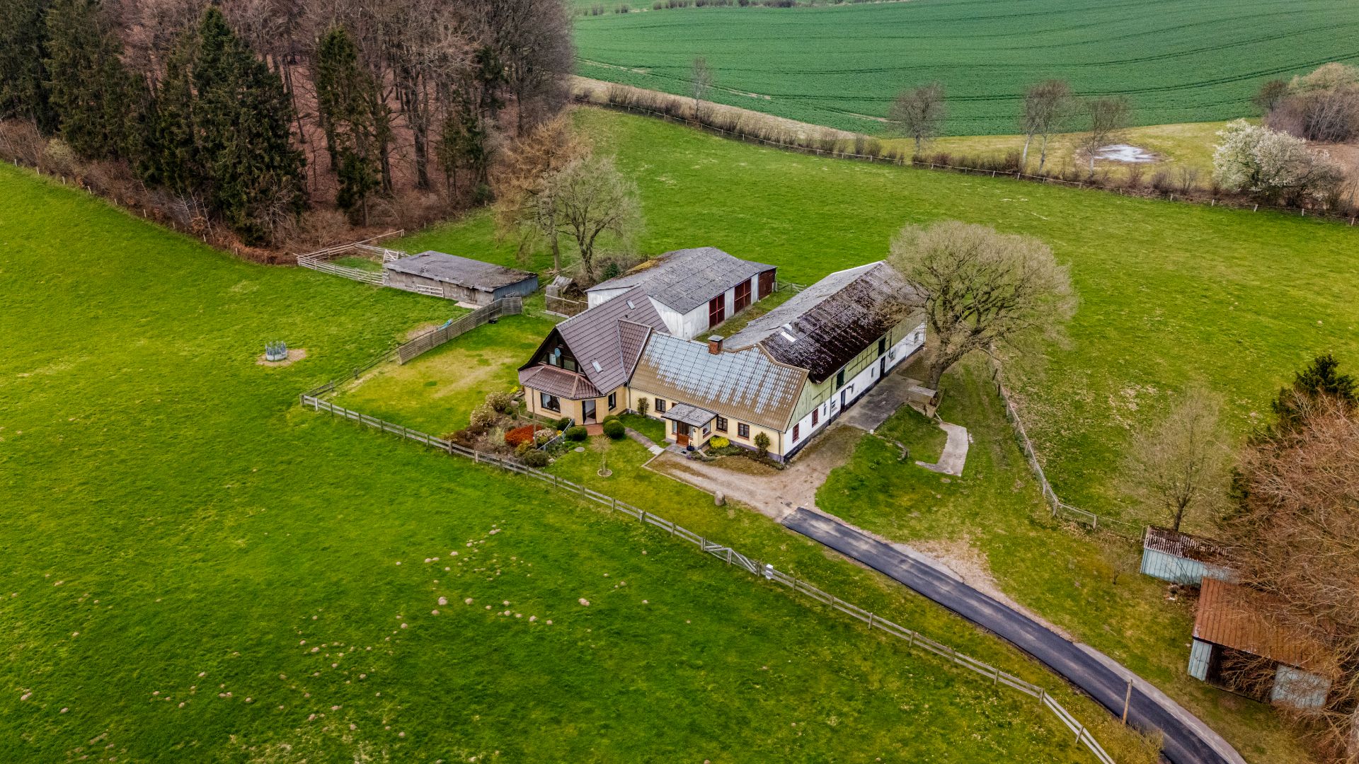 Luftaufnahme eines Landhauses mit Nebengebäuden und umzäunter Wiese in ländlicher Umgebung.