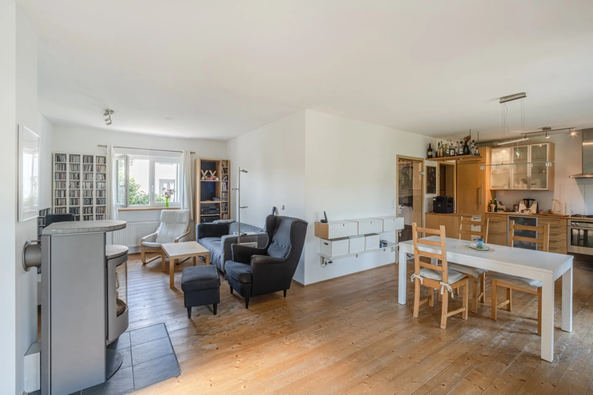Helles Wohnzimmer mit Holzboden, Kamin, Sitzbereich und offener Küche mit Esstisch.