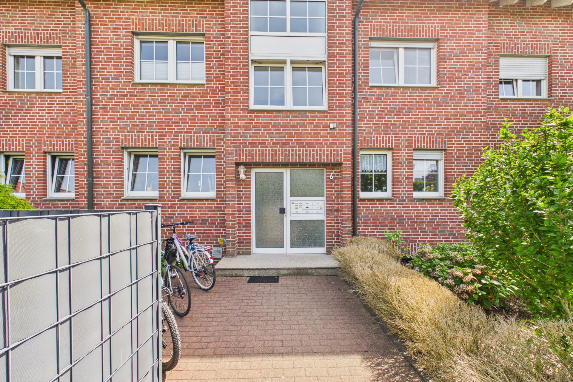 Eingang eines Backsteinhauses mit mehreren Fenstern und geparkten Fahrrädern davor.