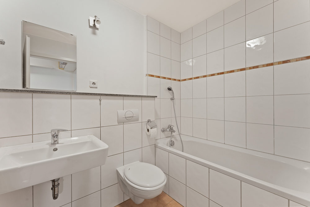 Helles Badezimmer mit weiß gefliester Wand, Badewanne, Waschbecken und Wandtoilette.