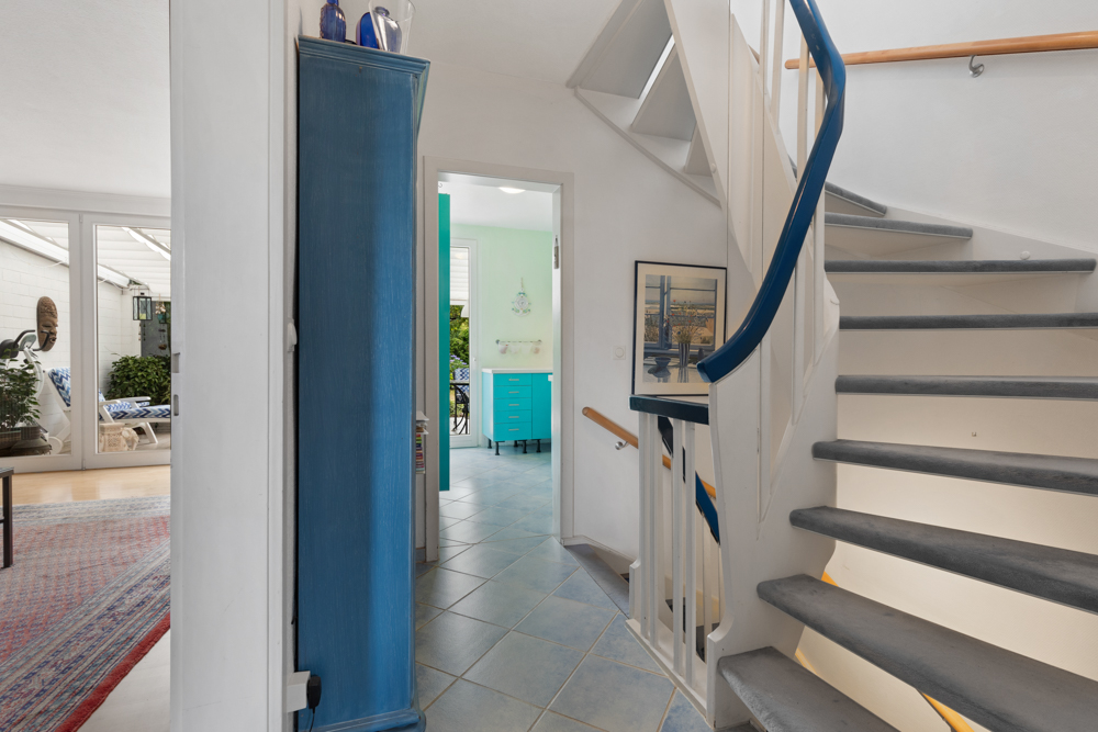 Flur mit blauer Treppe, blauem Schrank und Blick in ein helles Zimmer mit Fliesenboden.