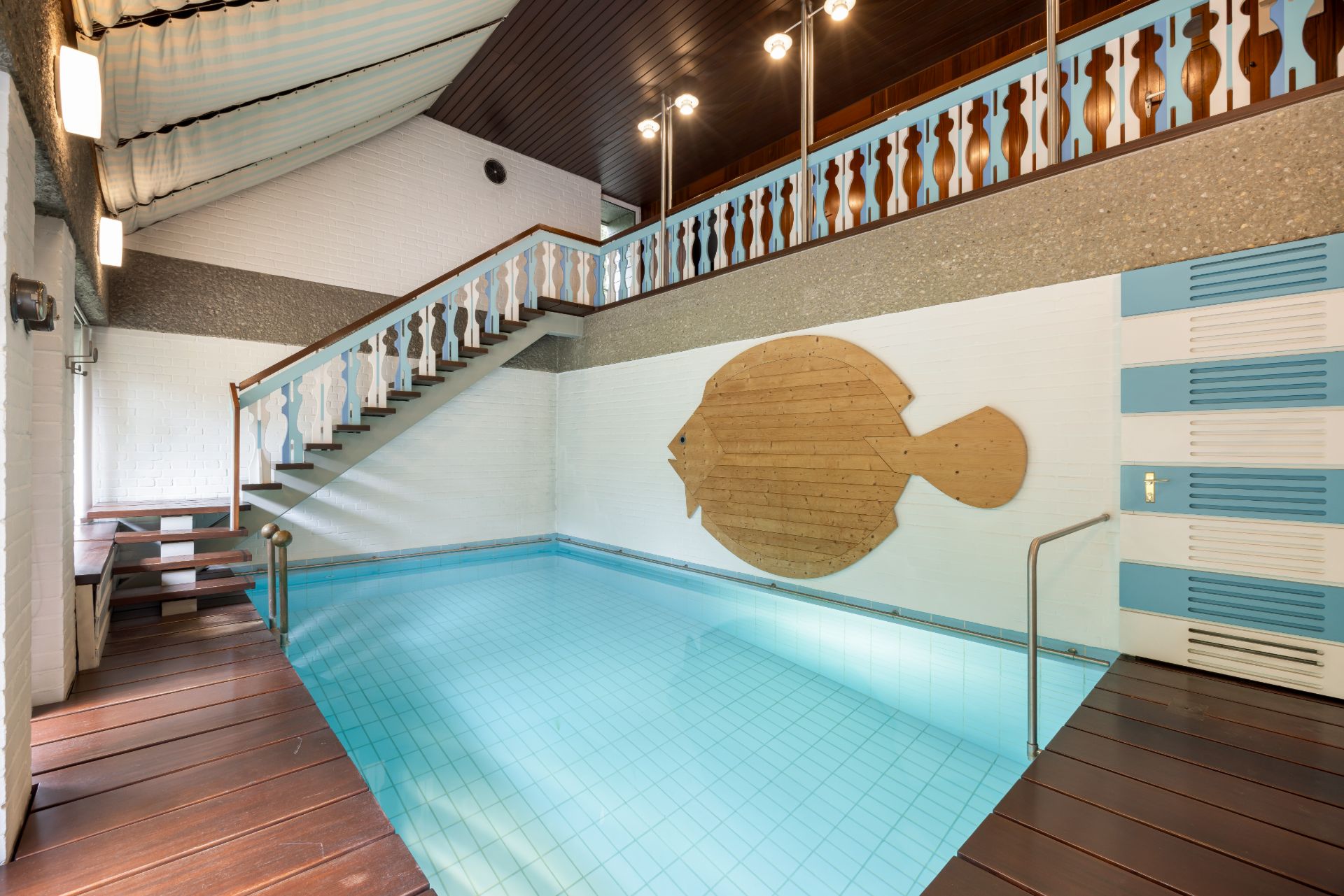 Innenpool mit Holztreppe, Geländer und Fischdekor an einer Wand.