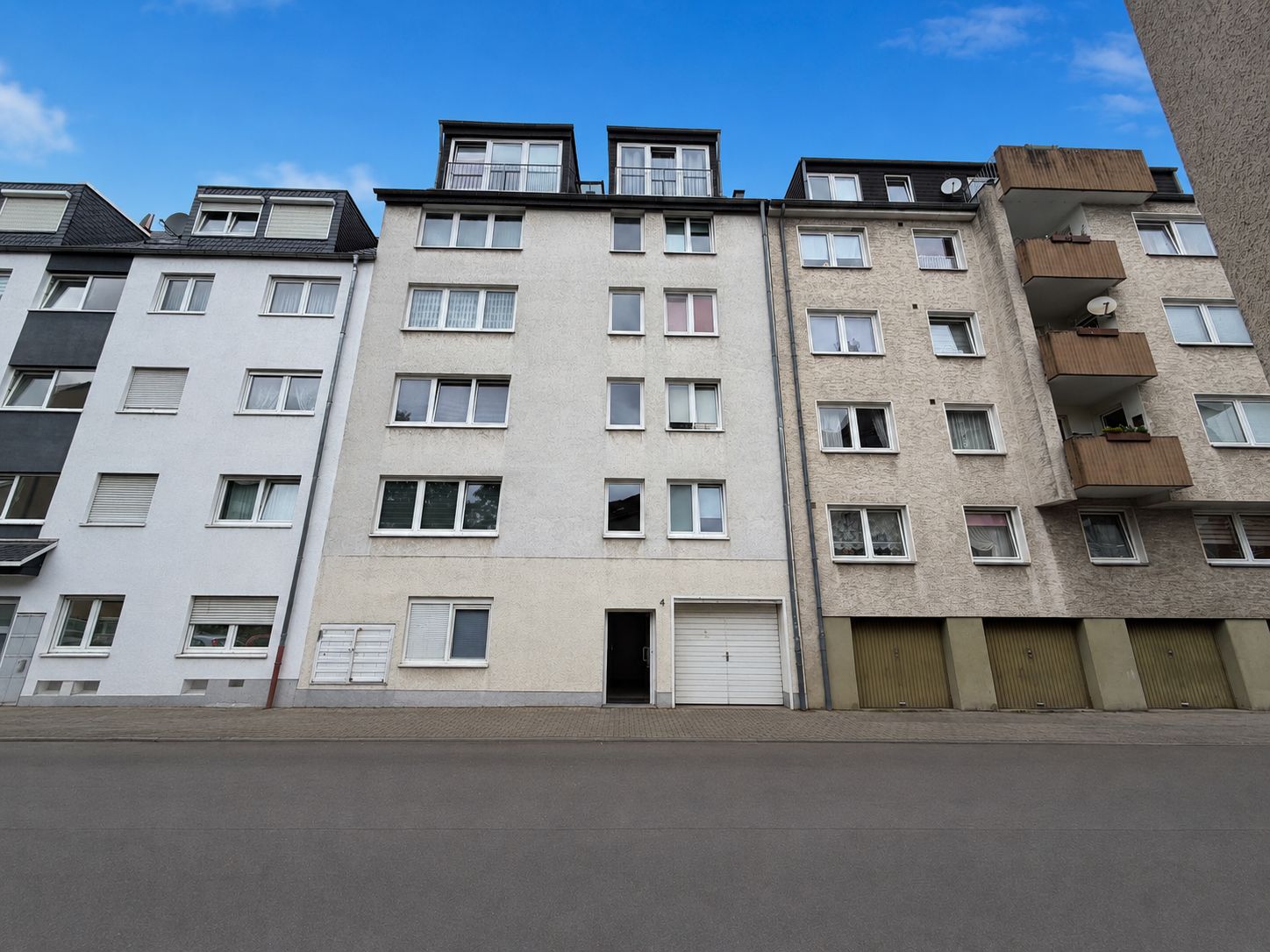 Mehrstöckiges Wohnhaus mit weißer Fassade, davor Straße, mehrere Fenster und Garagentor sichtbar.