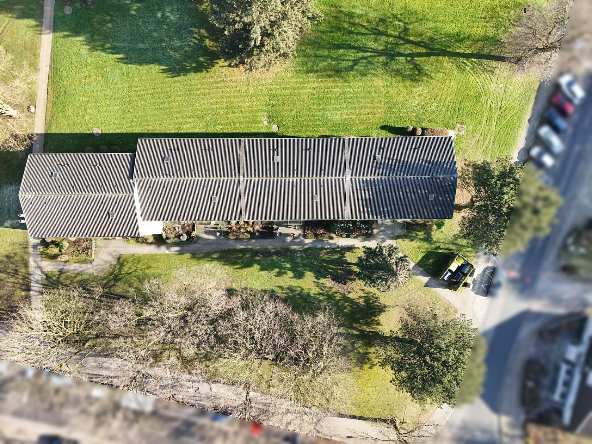 Luftaufnahme eines langen Wohngebäudes mit Gartenflächen und angrenzender Straße.
