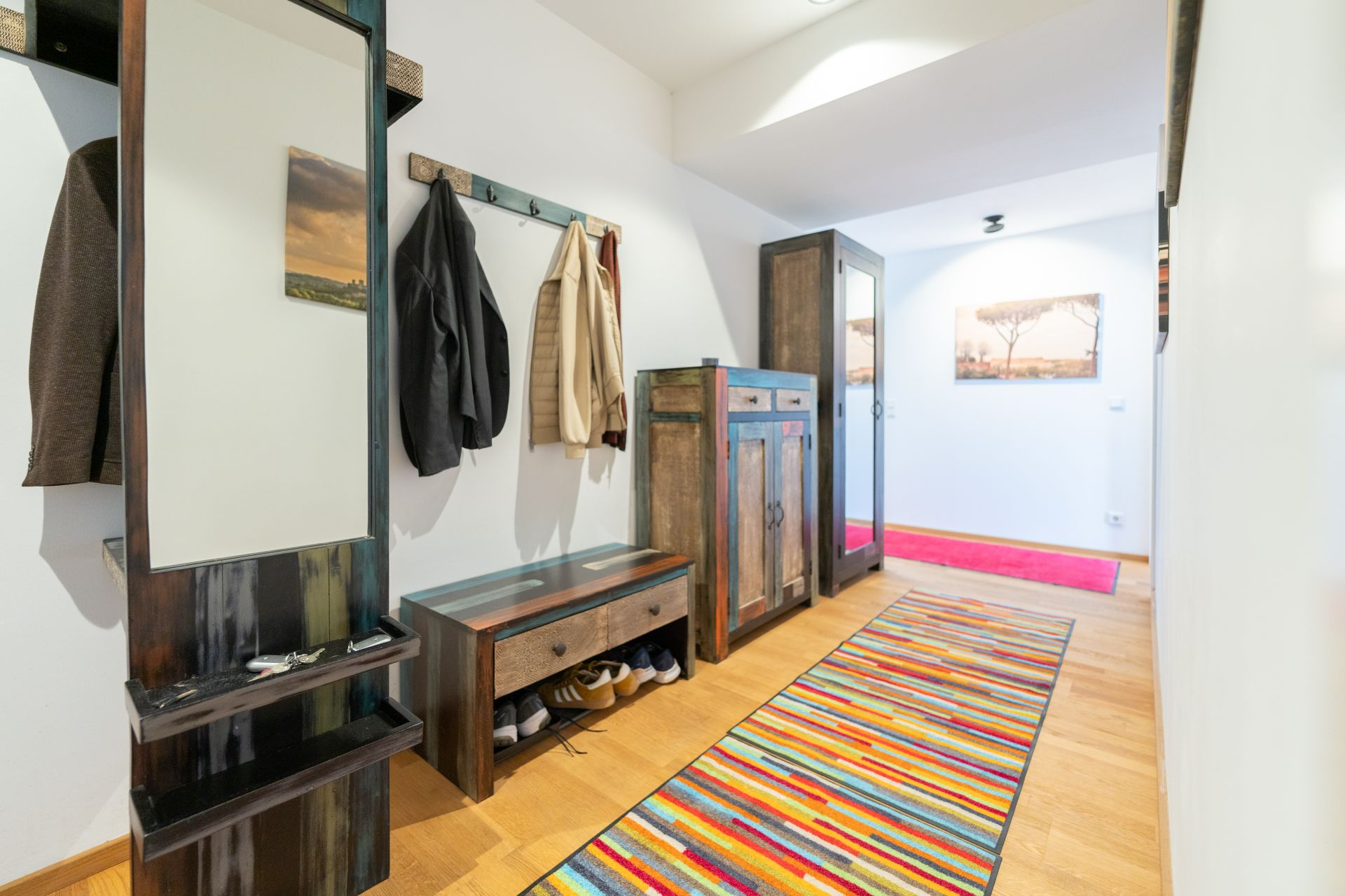 Heller Flur mit Garderobe, Spiegel, Schuhablage und buntem Teppich auf Holzboden.