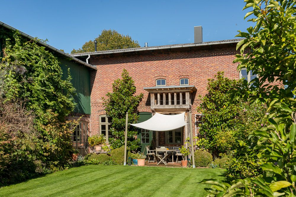 Backsteinwohnhaus mit Terrasse, Sonnensegel und grünem Garten bei Sonnenschein.