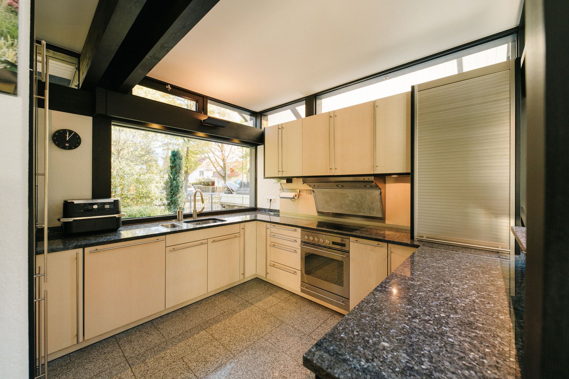 Moderne Küche mit großen Fenstern, heller Arbeitsplatte und eingebauten Schränken.