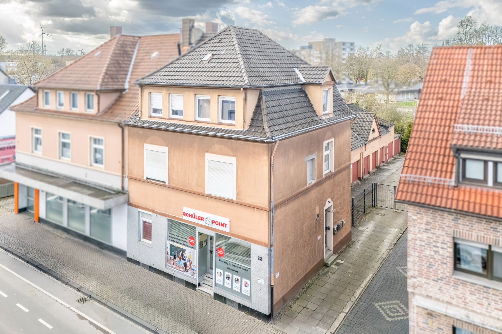Dreistöckiges Wohngebäude mit Geschäft im Erdgeschoss und brauner Fassade an einer Straße.
