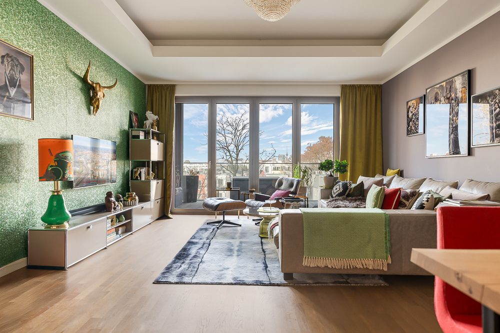 Modernes Wohnzimmer mit großem Sofa, Teppich, TV, Dekoration und Fensterfront mit Blick nach draußen.