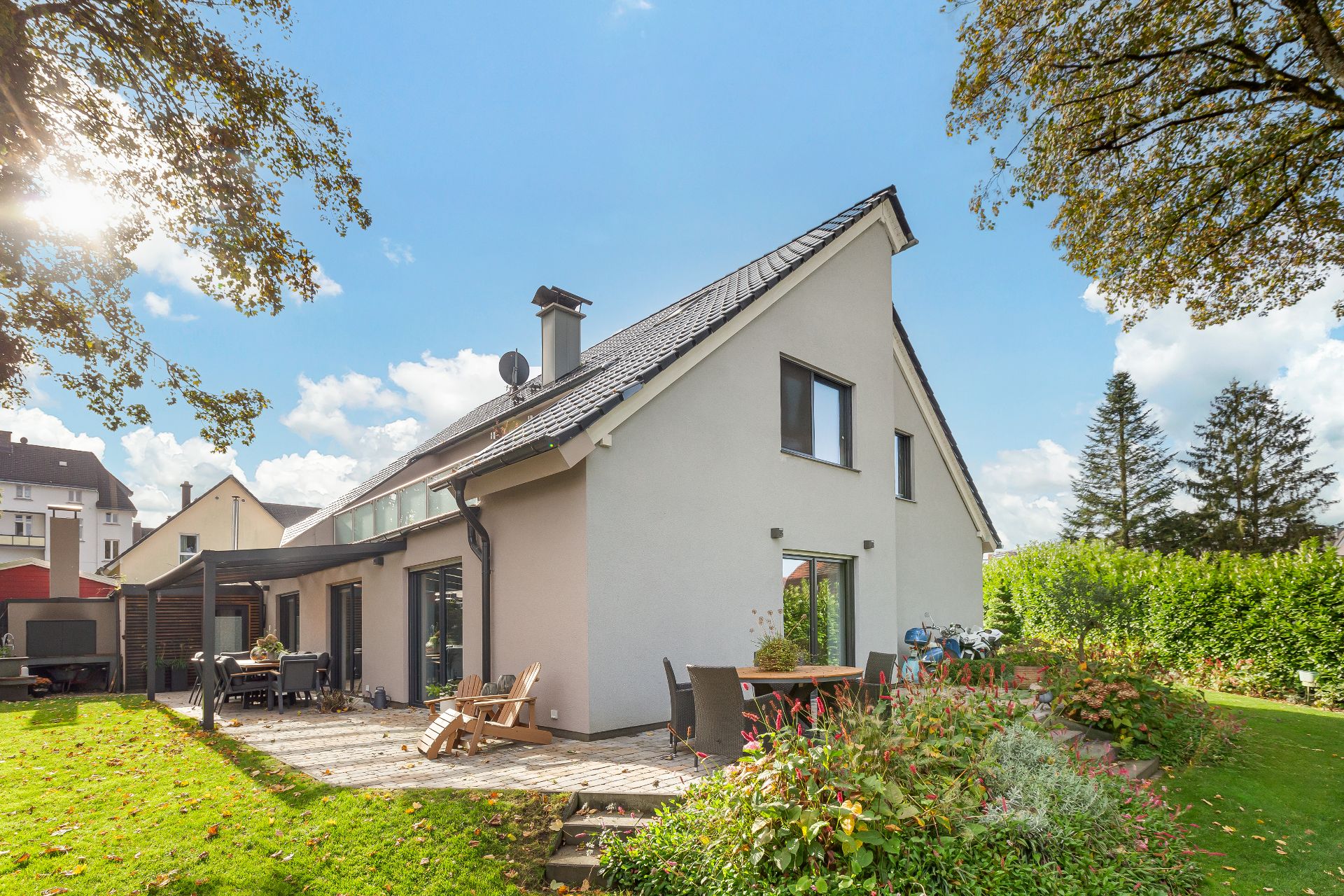 Modernes Einfamilienhaus mit Terrasse, Gartenmöbeln und gepflegtem Garten bei Sonnenschein.